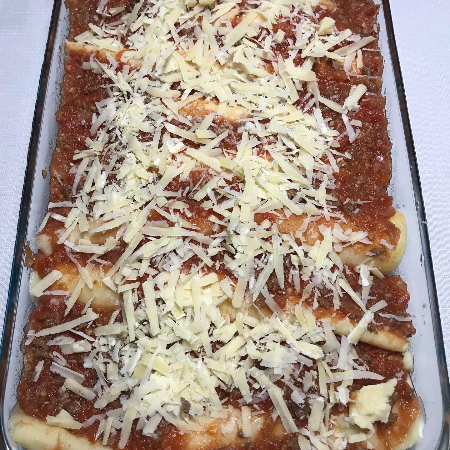 Panqueque salado sin gluten, listo y relleno de carne molida, acompañado de salsa de tomate casera, terminado con queso parmesano rallado.